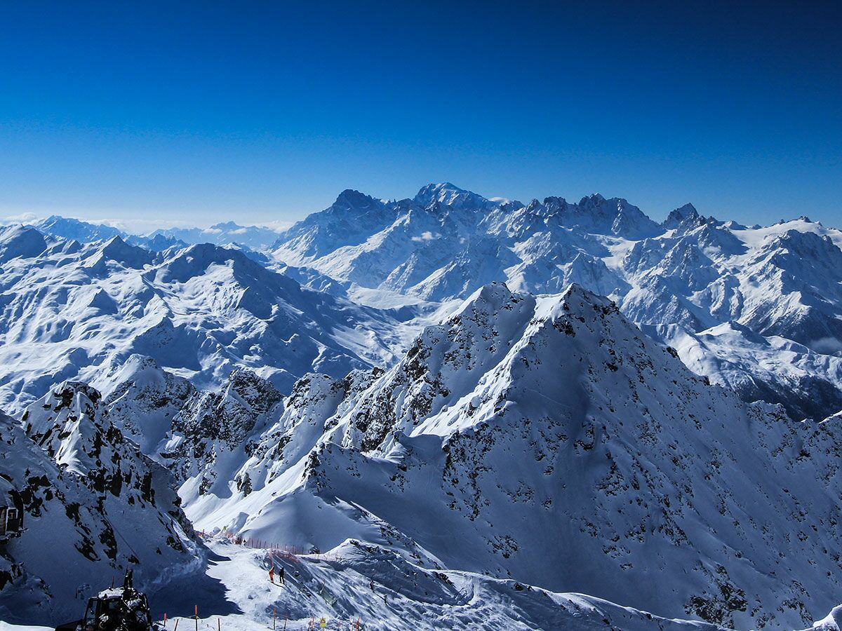 Majestätische schneebedeckte Berge und Täler einer Winterlandschaft unter blauem Himmel mit Skifahrern in den Alpen.