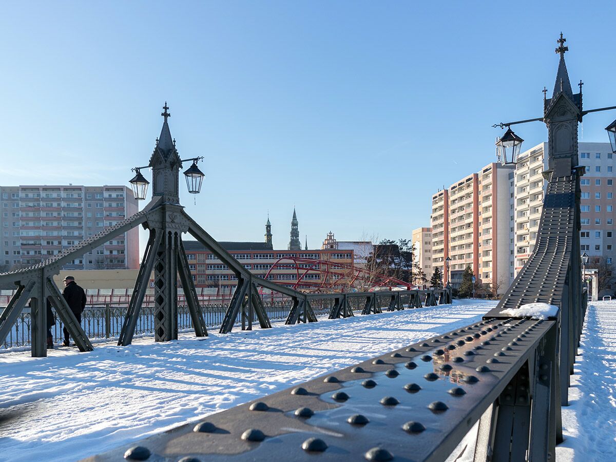 Eine schneebedeckte Brücke mit historischen Laternen und Stadtgebäuden im Winter unter blauem Himmel.