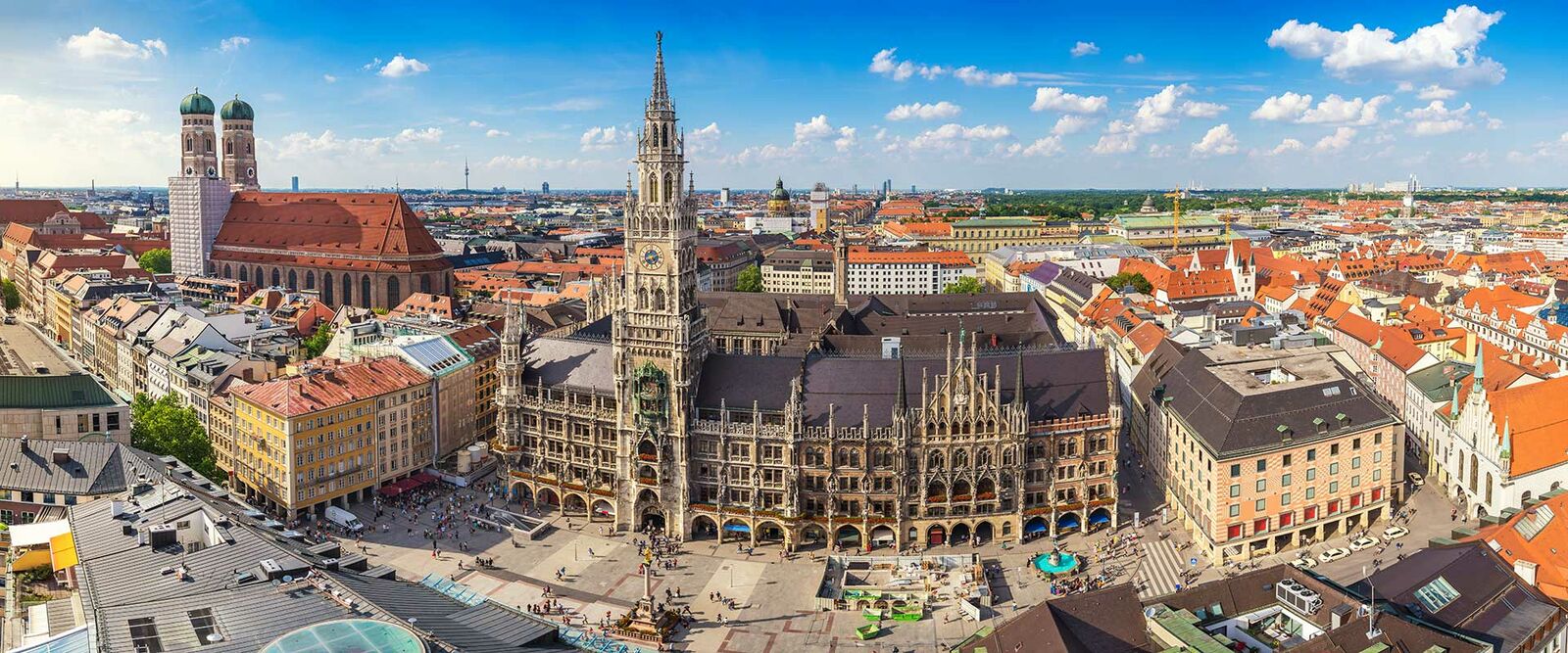 Panoramablick auf Münchens Marienplatz mit dem Neuen Rathaus und der Frauenkirche unter blauem Himmel.