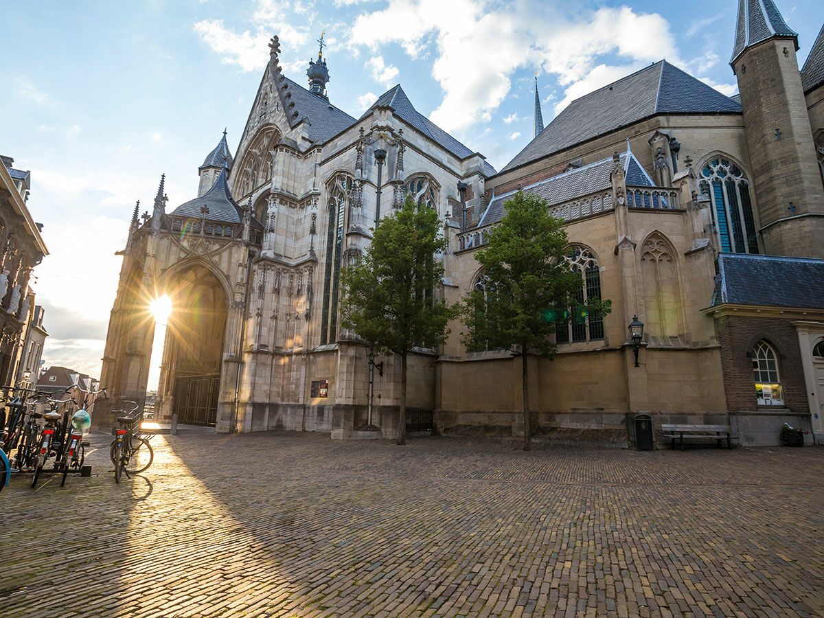 Historische gotische Domkirche in Utrecht mit blendenden Sonnenstrahlen durch einen Bogen, die den Kopfsteinpflasterplatz und Fahrräder beleuchten.