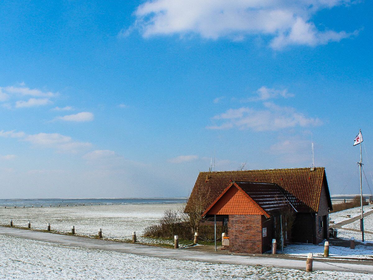 Rotes Backsteinhaus mit braunem Dach im Schnee an der Küste unter blauem Himmel mit Wolken, Blick auf das Meer.