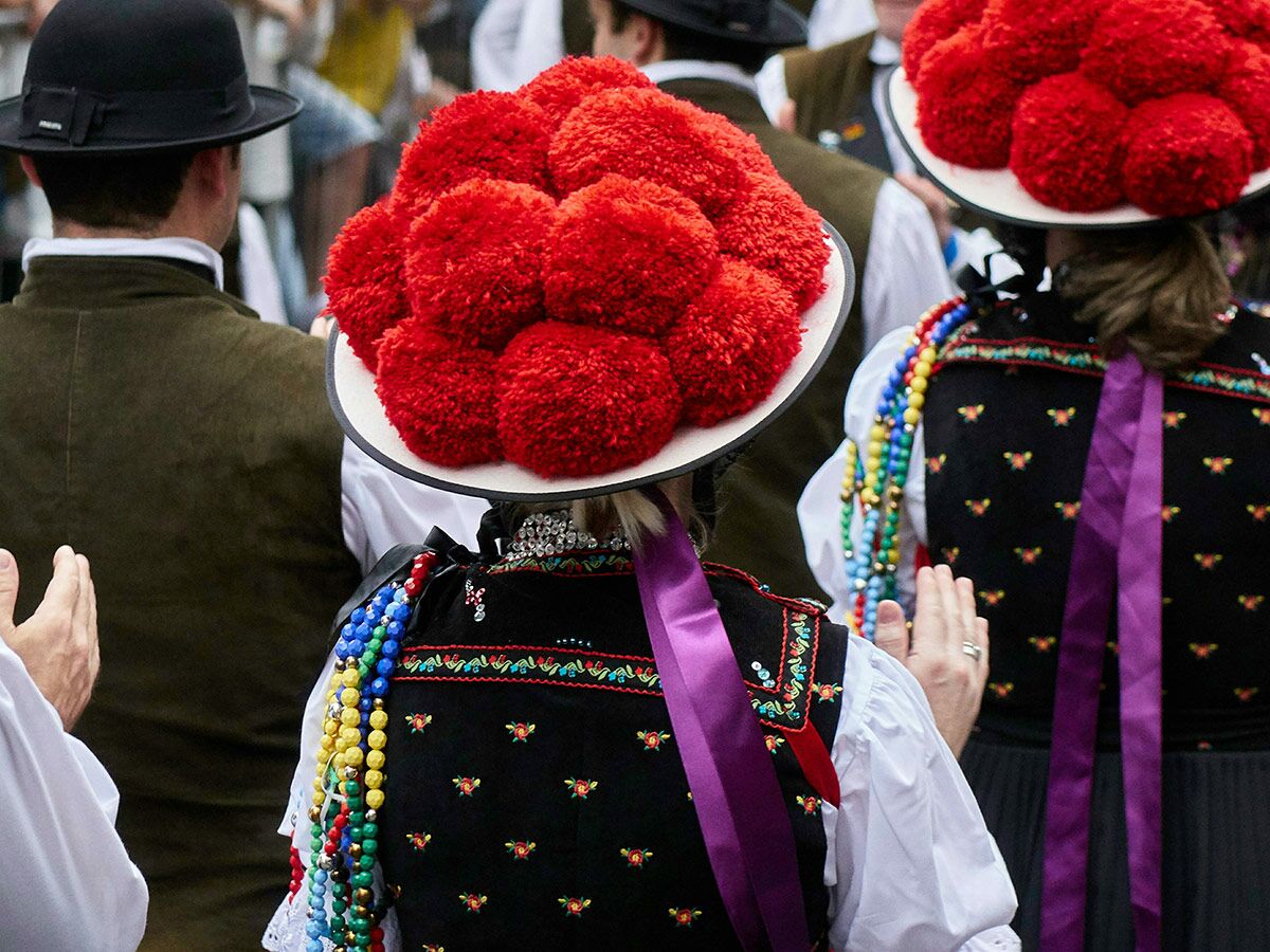 Rückansicht von Personen in traditioneller Schwarzwälder Tracht mit roten Bollenhüten, bestickten Westen und bunten Perlenketten bei einem Fest.