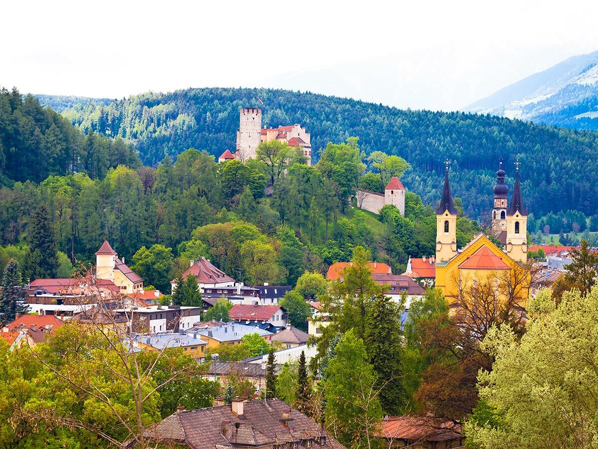 Blick auf eine historische europäische Stadt mit Schloss auf einem Hügel, Kirche und grünen Wäldern.