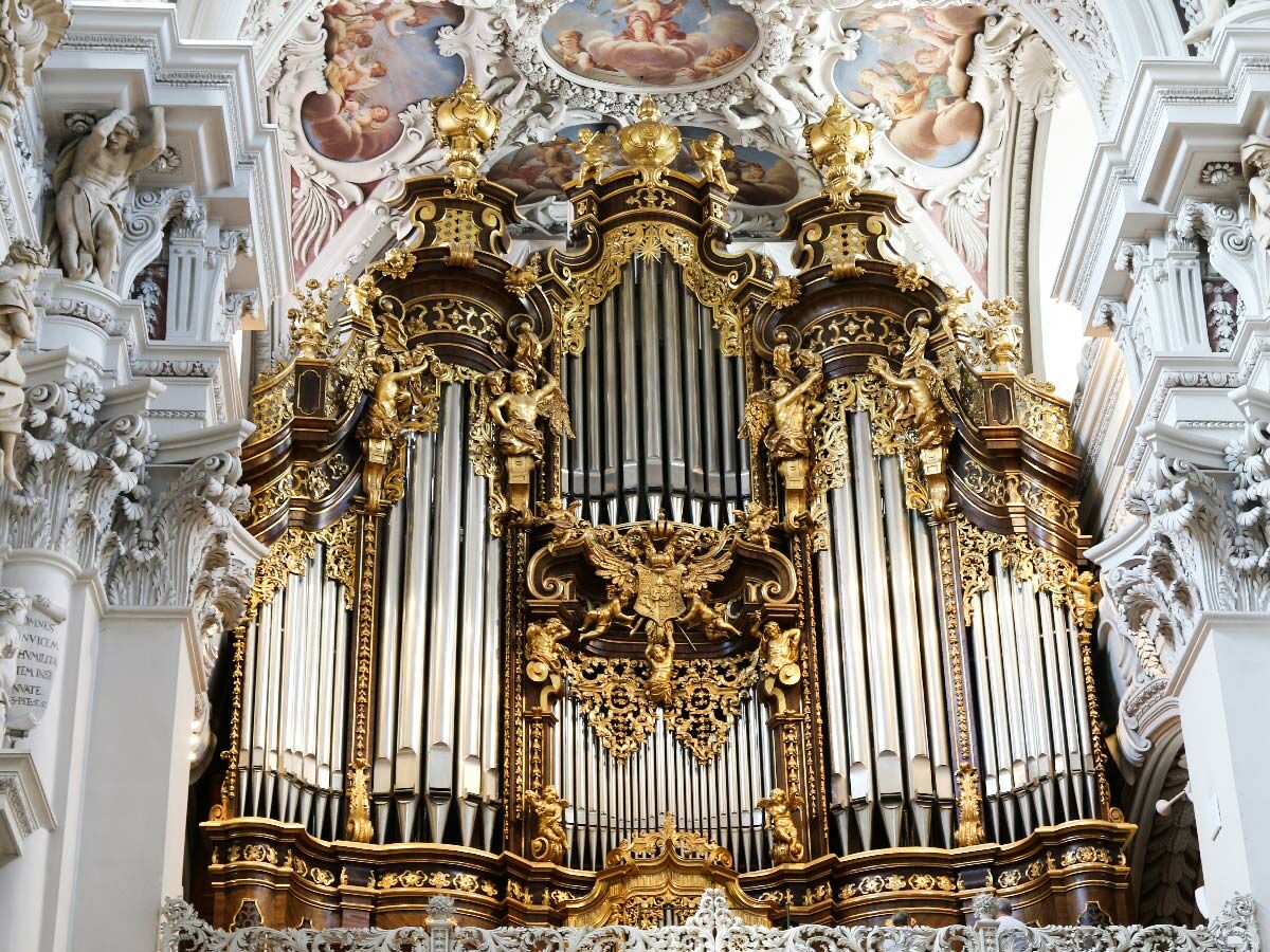 Prunkvolle, vergoldete Barockorgel in einer Kirche, umgeben von detaillierten Stuckarbeiten, Engelfiguren und historischen Deckenfresken.