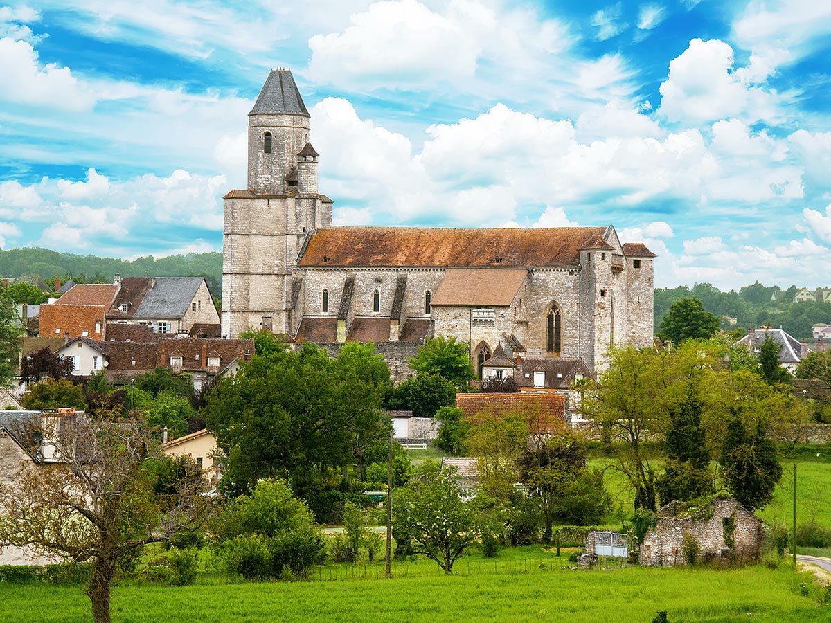 Historische Steinkirche mit hohem Turm in malerischem französischem Dorf, umgeben von grüner Landschaft unter blauem Himmel.