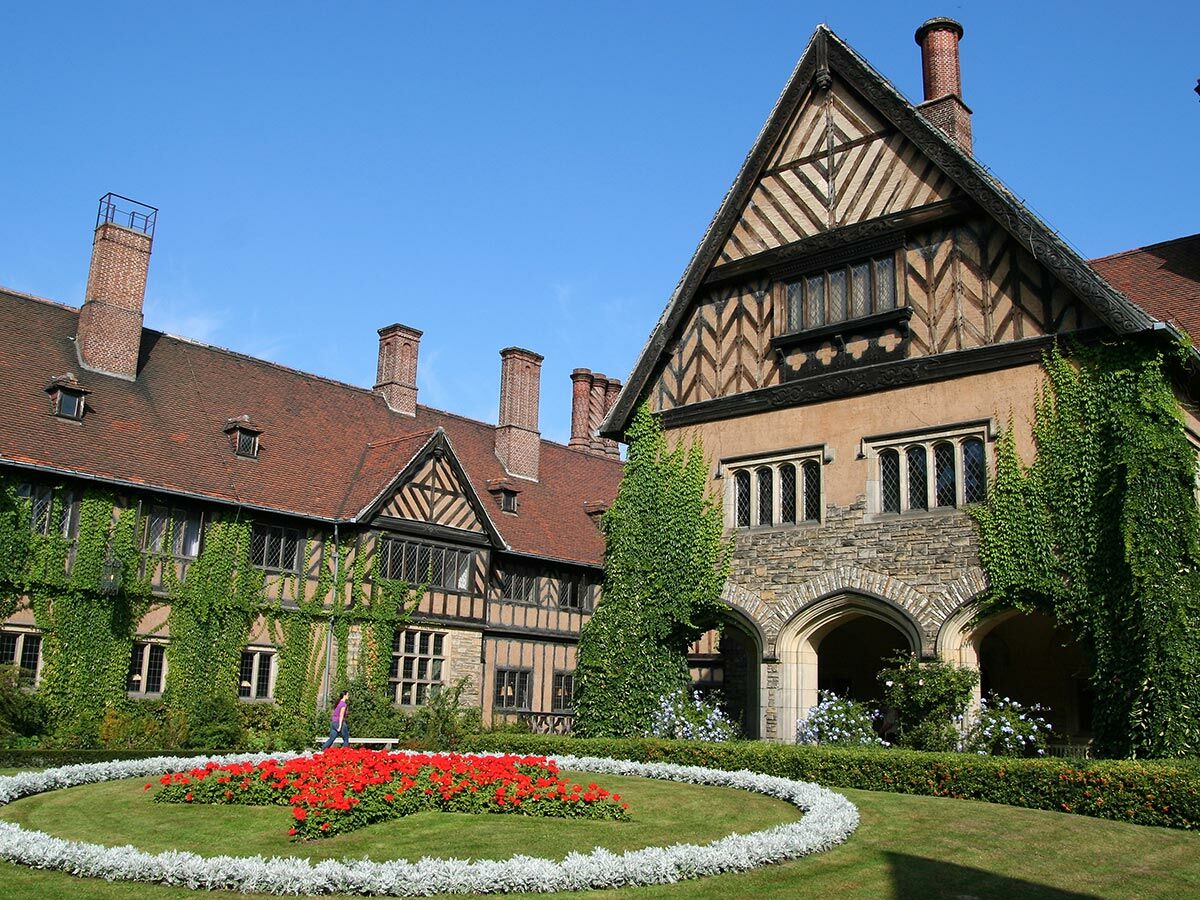 Historisches Schlossgebäude mit Fachwerk, Efeu bewachsenen Wänden, roten Ziegeldächern, markanten Schornsteinen und einem gepflegten Garten.