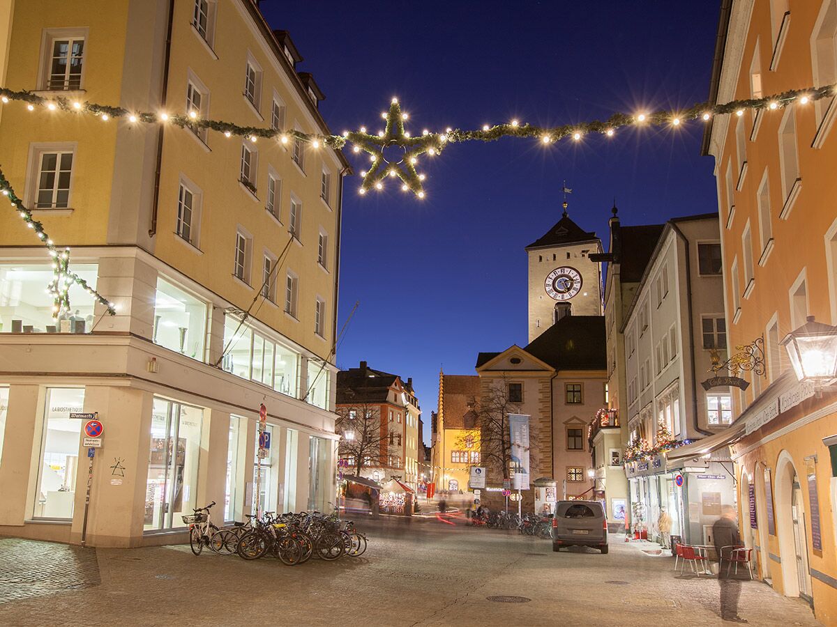 Festlich beleuchtete Altstadtgasse bei Nacht mit historischem Uhrturm, bunten Häusern, Lichterketten und parkenden Fahrrädern.