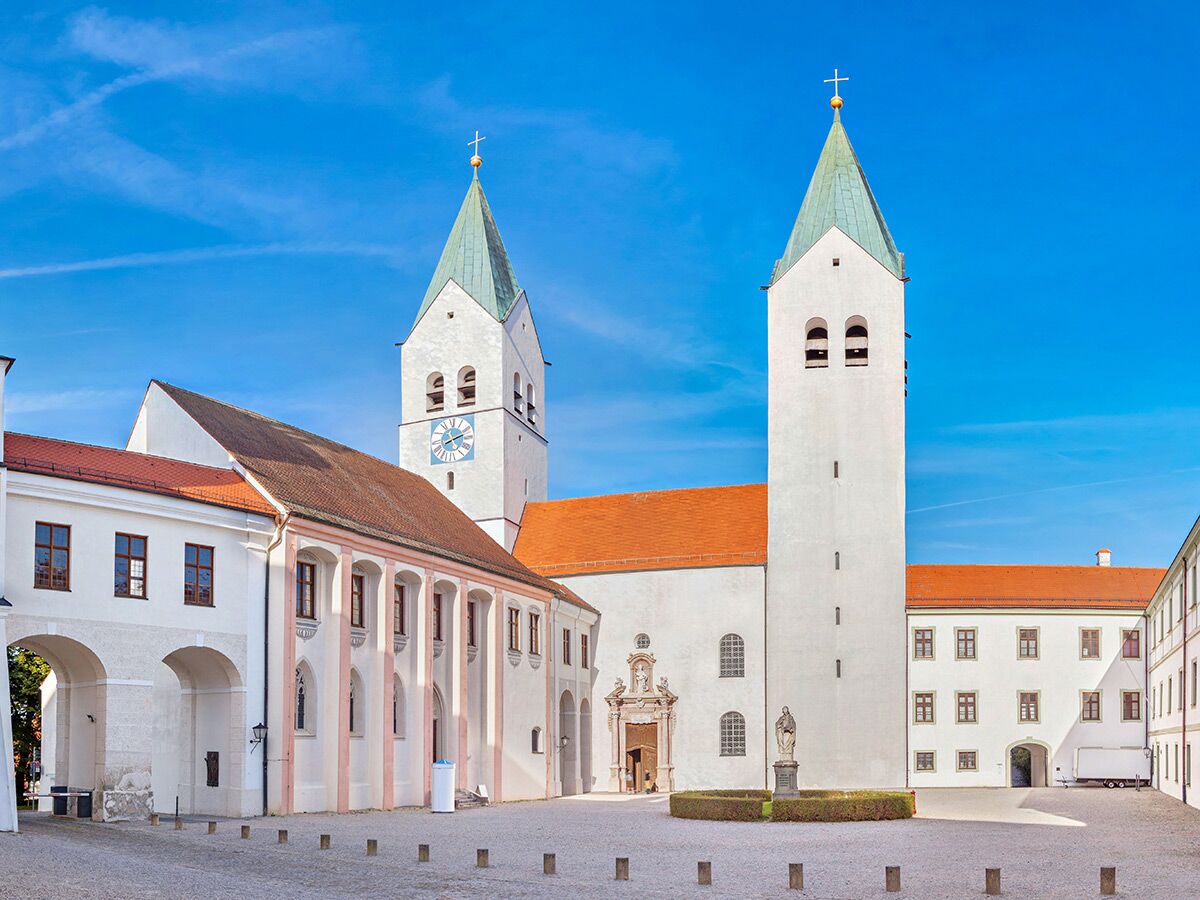 Historisches Kloster Benediktbeuern mit zwei Kirchtürmen, Uhr und roten Dächern unter blauem Himmel in Bayern.