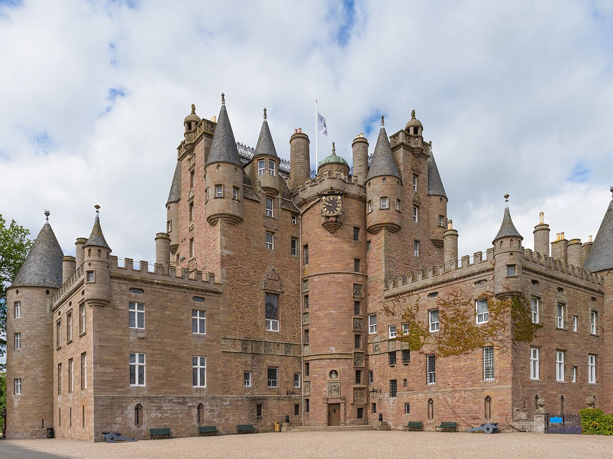 Das historische Glamis Castle in Schottland mit seinen zahlreichen Türmen, spitzen Dächern und einer Uhr an einem bewölkten Tag.