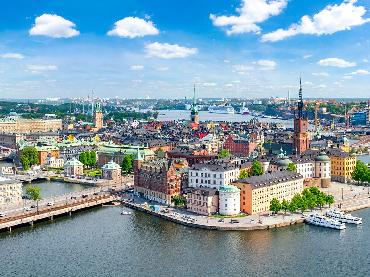 Luftaufnahme der schwedischen Hauptstadt Stockholm mit Gamla Stan, historischen Gebäuden, Kirchen, Booten und Brücken am Wasser unter blauem Himmel.