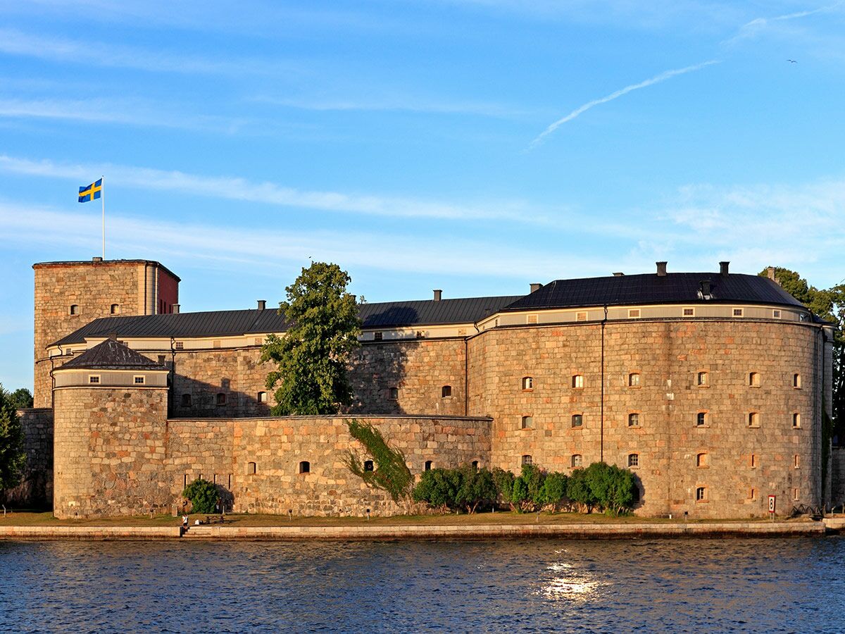 Historische Steinfestung Vaxholm in Schweden am Wasser unter blauem Himmel mit wehender schwedischer Flagge.