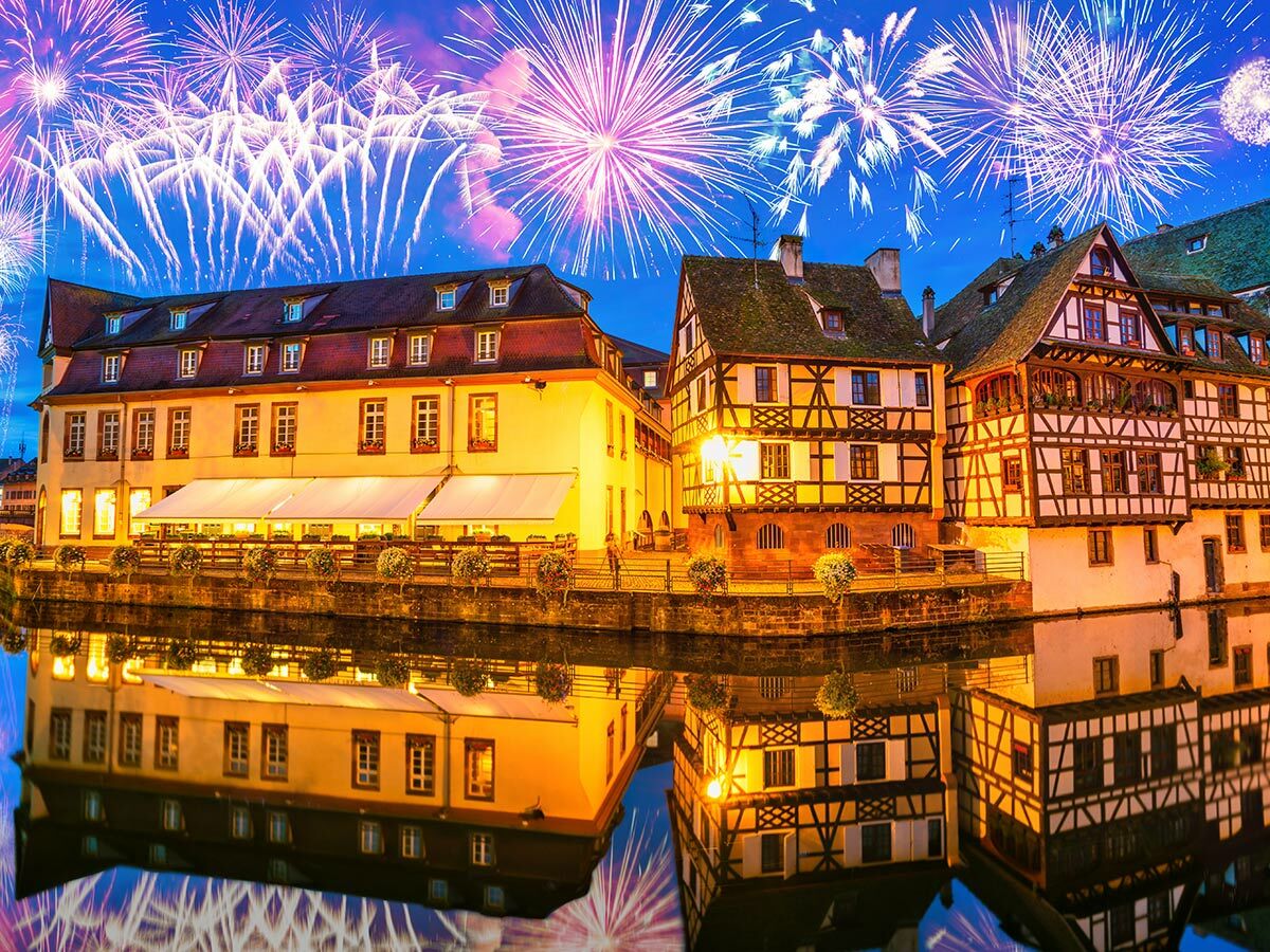 Historische Fachwerkhäuser in Strasbourg, Petite France, am Kanal bei Nacht. Buntes Feuerwerk und Reflexionen im Wasser.