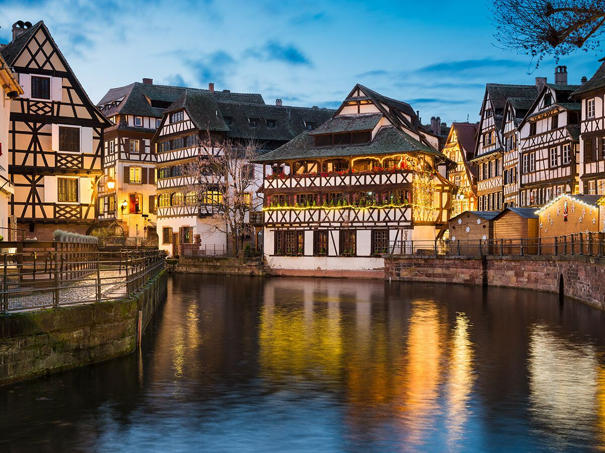 Abendansicht von Fachwerkhäusern in Straßburg, La Petite France, mit Lichtern, die sich im Kanal spiegeln.