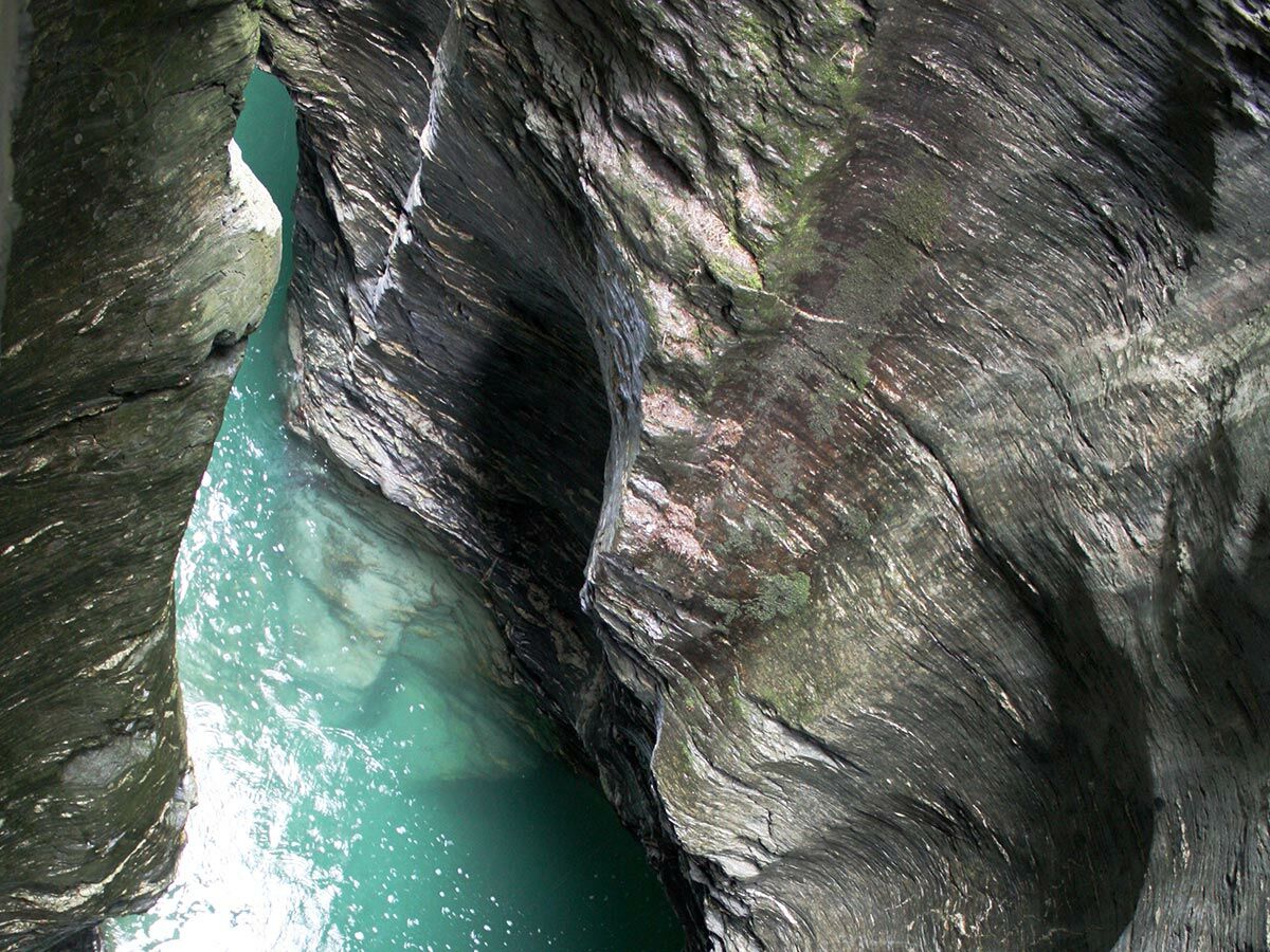 Blick in eine tiefe, enge Schlucht mit leuchtend türkisem Flusswasser, umgeben von geschichteten Felswänden.