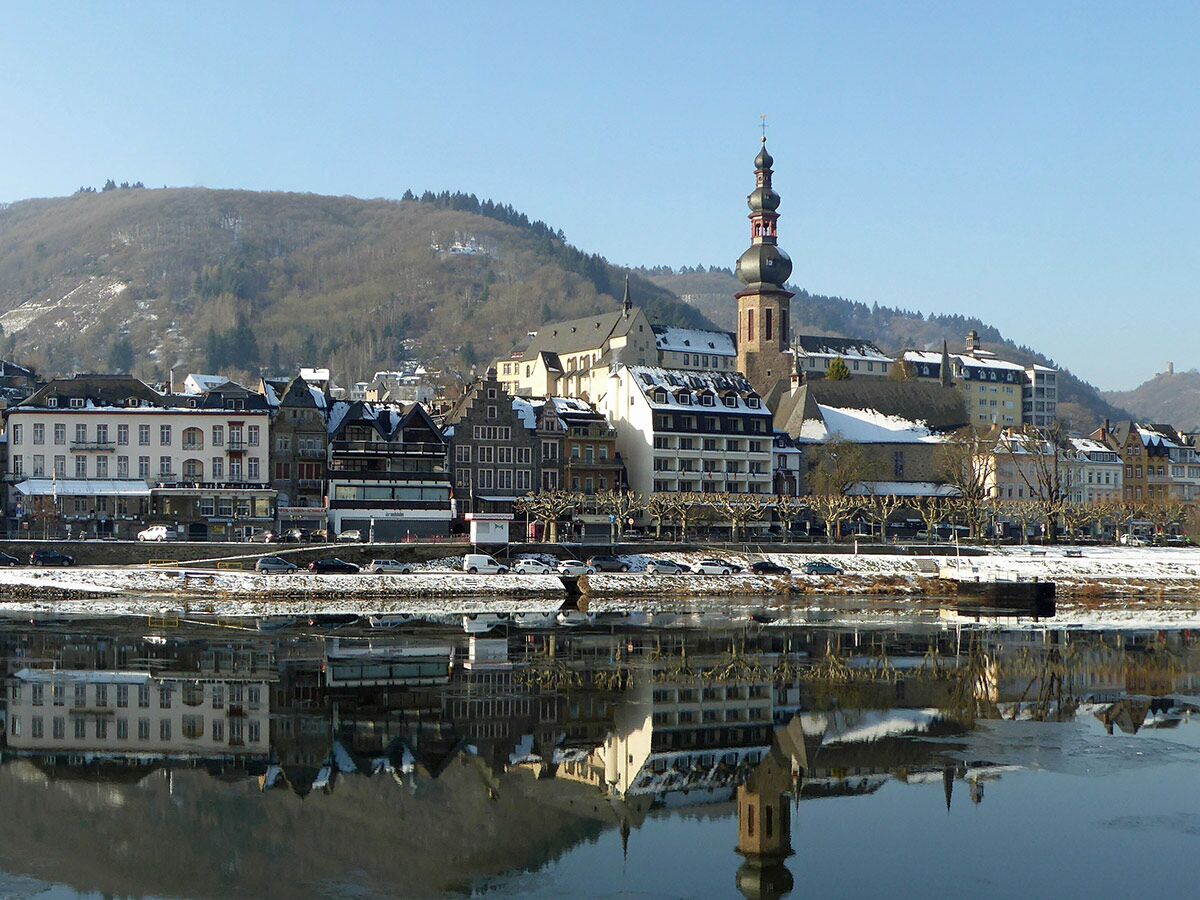 Winterliche Stadt am Fluss in Deutschland mit historischen Gebäuden, markanter Kirche und Schnee auf Hügeln.