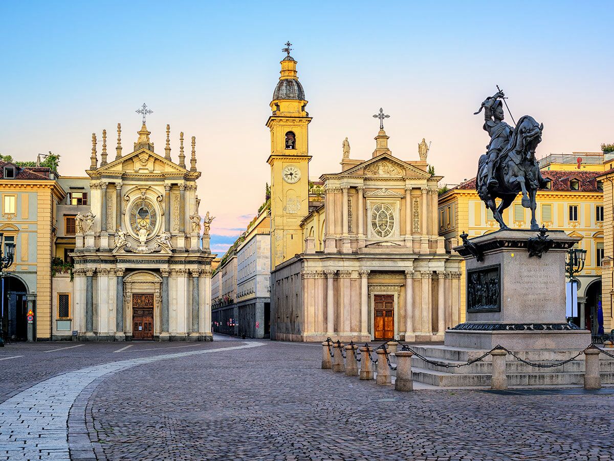 Großer, leerer Piazza San Carlo in Turin mit barocken Kirchen, Glockenturm und Reiterstatue im Morgenlicht.
