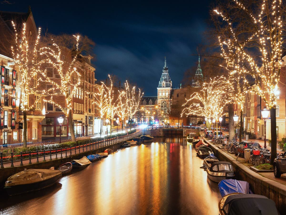 Festlich beleuchtete Amsterdamer Gracht bei Nacht im Winter mit historischen Gebäuden, Booten und spiegelnden Lichtern.