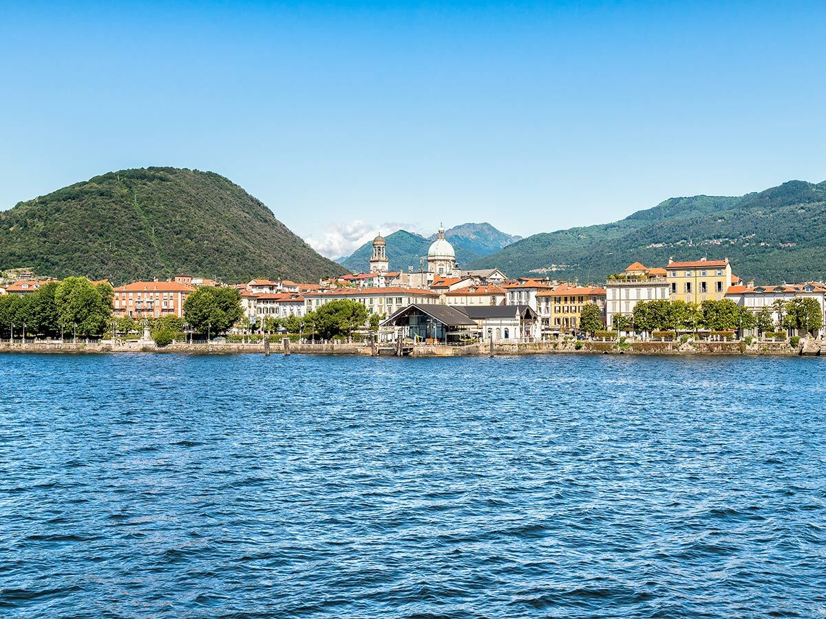 Panoramablick auf Intra Verbania am Lago Maggiore in Italien mit Basilika San Vittore, farbigen Gebäuden und grünen Bergen.