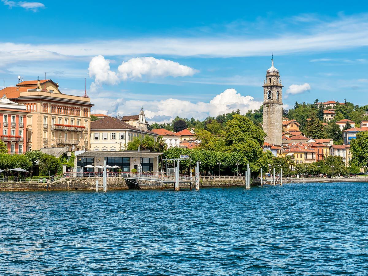 Panorama von Pallanza am Lago Maggiore mit bunten Gebäuden, Glockenturm, Pier und blauem Himmel.