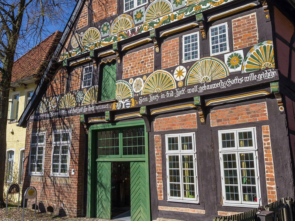 Historisches Fachwerkhaus mit dunkelbraunen Holzbalken, roten Ziegeln und reich bemalter, gelb-grüner Fassade in Norddeutschland.