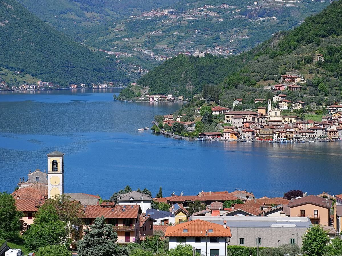 Panoramablick auf den Iseosee mit dem malerischen Dorf Peschiera Maraglio am Ufer und grünen Bergen.