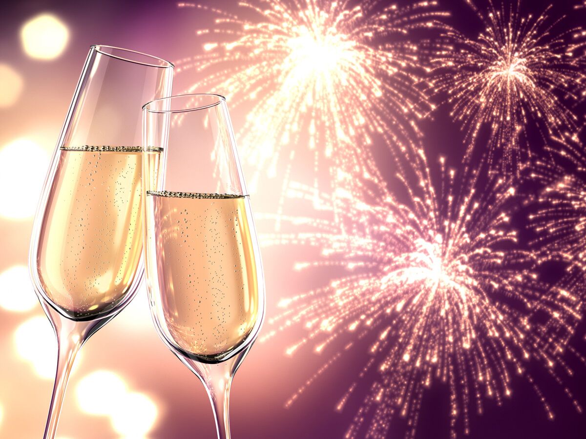 Zwei Champagner-Gläser stoßen vor einem Hintergrund aus funkelndem Feuerwerk und Bokeh-Lichtern an, symbolisieren Feier und Neujahr.