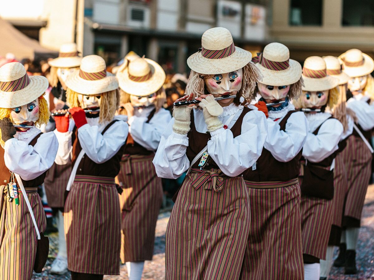 Gruppe maskierter Fasnachtsmusiker in traditionellen Kostümen mit Strohhüten spielt Flöten während eines Umzugs.