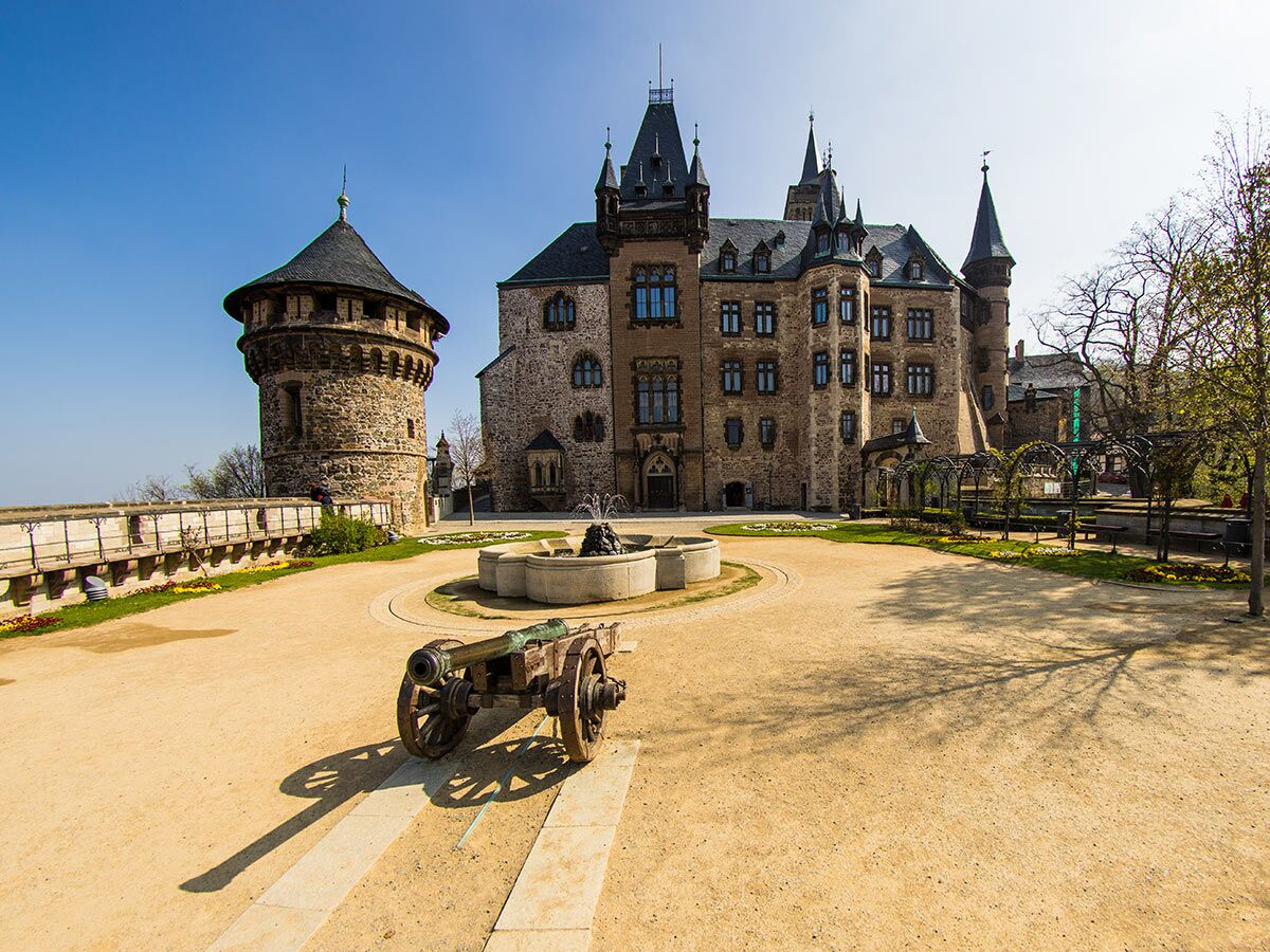 Blick auf Schloss Wernigerode im Harz mit Steinburg, Turm, Innenhof, Kanone und Brunnen an einem sonnigen Tag.