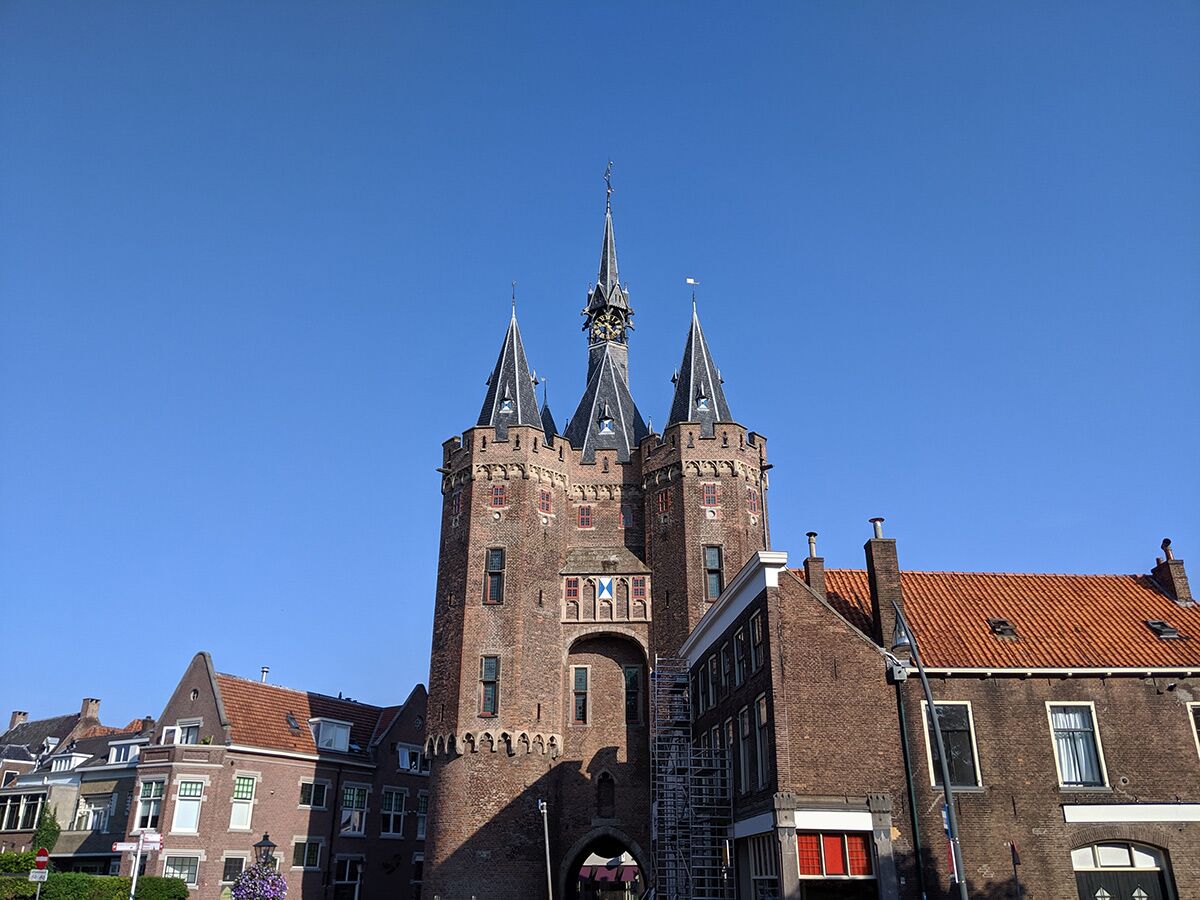 Historische Oostpoort (Osttor) in Delft, Niederlande, mit Backsteintürmen unter blauem Himmel, umgeben von alten Gebäuden.