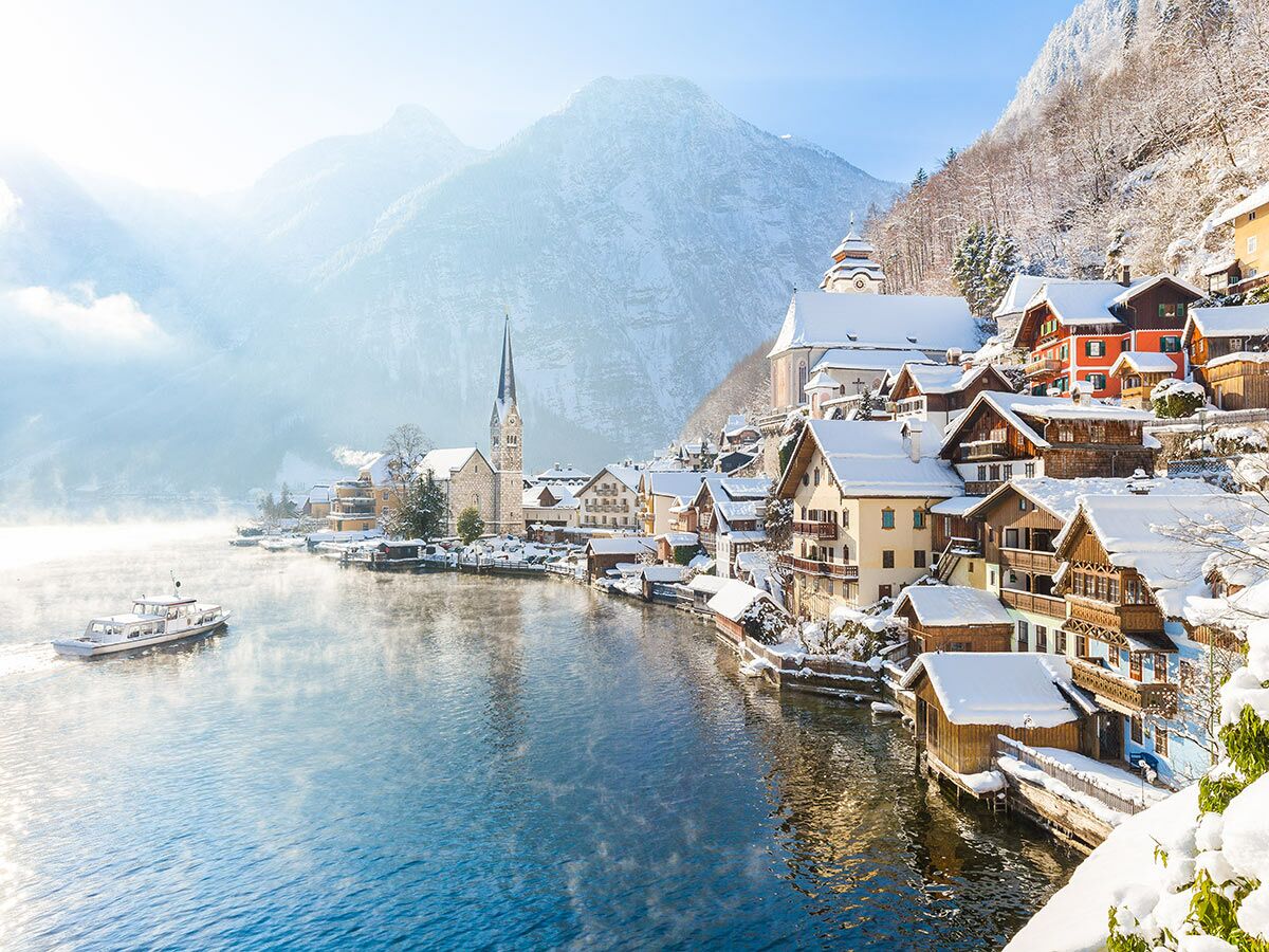 Malerisches Hallstatt im Winter mit verschneiten Häusern, Kirche und See, umgeben von schneebedeckten Bergen.