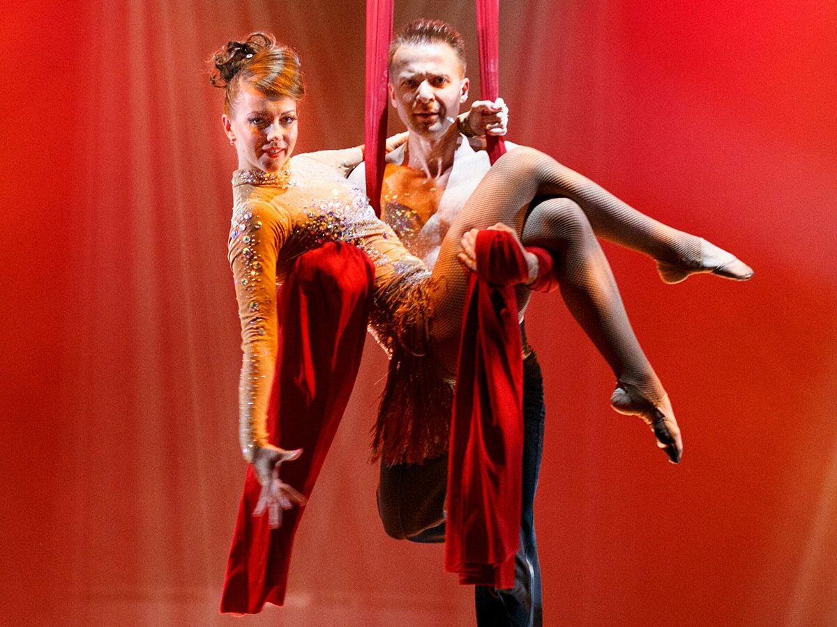 Zwei Luftakrobaten, Mann und Frau, präsentieren eine artistische Performance mit roten Tüchern vor rotem Hintergrund, voller Anmut und Stärke.