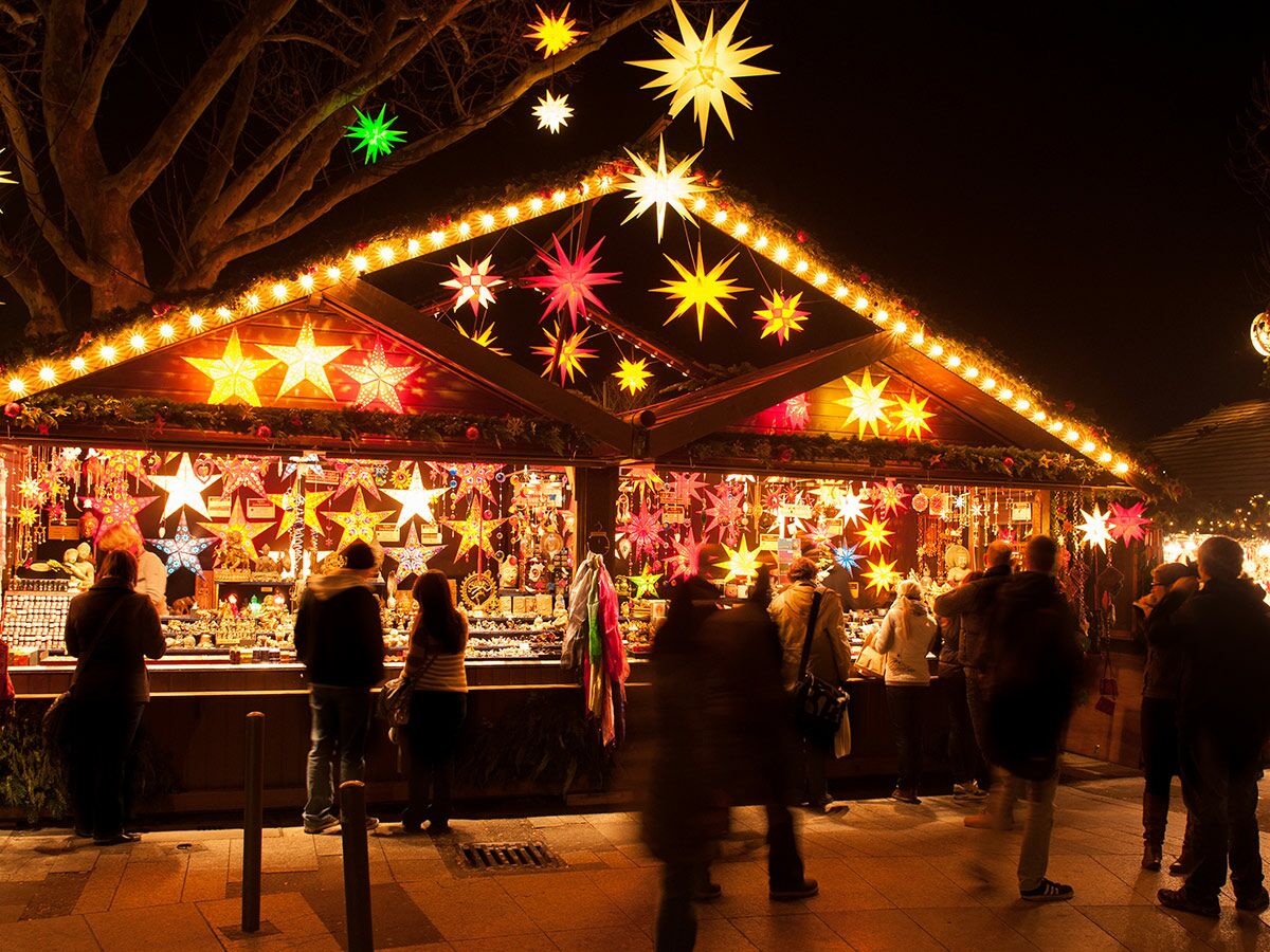 Weihnachtsmarkt bei Nacht mit beleuchteten Ständen und vielen leuchtenden Sternen, Menschen bummeln und kaufen ein.