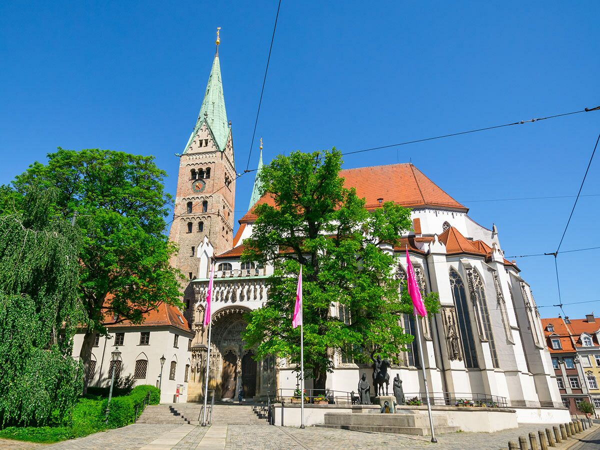 Ansicht des historischen Bremer Doms St. Petri mit grünem Turmdach, Uhr und Backsteinfassade unter blauem Himmel, umgeben von Bäumen und Statuen.