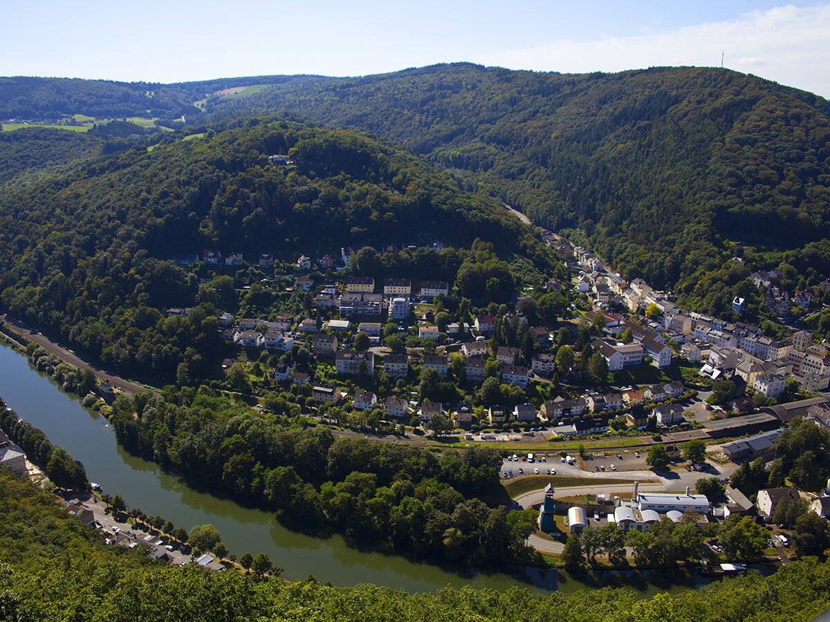 Luftaufnahme einer idyllischen Stadt im grünen Flusstal, umgeben von dichten Wäldern und einem malerischen Flusslauf.