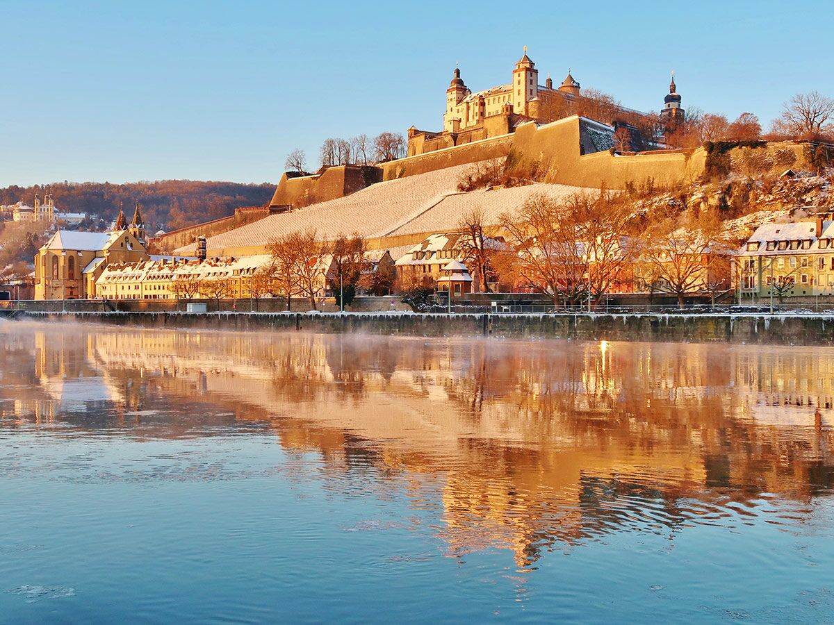 Panoramablick auf die Festung Marienberg und den Main in Würzburg im Winter bei Sonnenaufgang, mit goldenen Reflexionen.