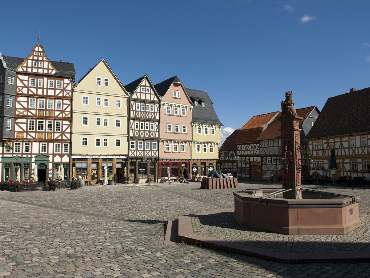 Sonniger historischer Marktplatz mit bunten Fachwerkhäusern, Kopfsteinpflaster und Brunnen mit Löwenstatue in deutscher Altstadt.
