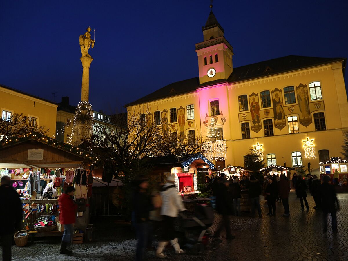 Festlicher Weihnachtsmarkt auf historischem Rathausplatz bei Abenddämmerung mit Lichterketten, Ständen, Menschen und beleuchtetem Rathaus.