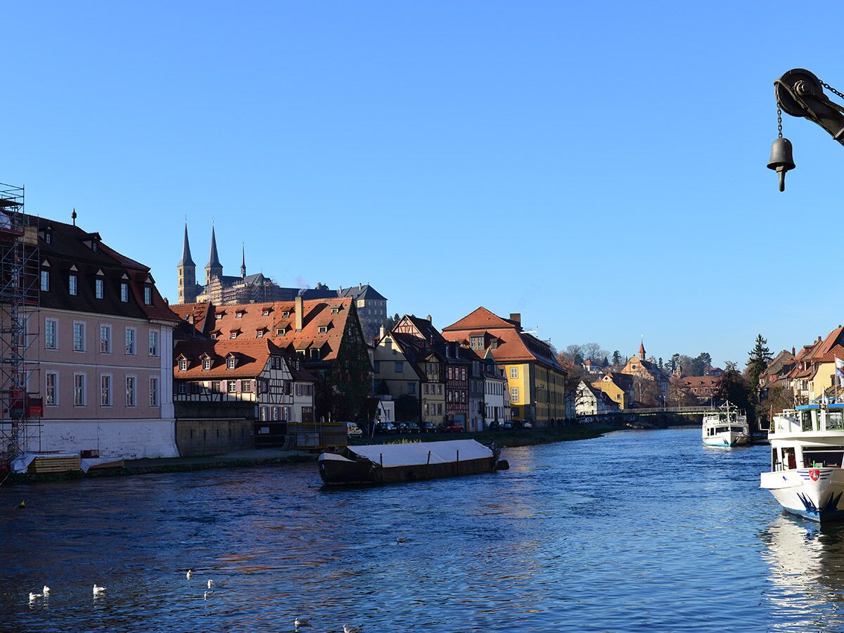 Historische Altstadt von Bamberg am Fluss Regnitz mit Dom im Hintergrund. Mehrere Boote und alte Gebäude säumen das Ufer.