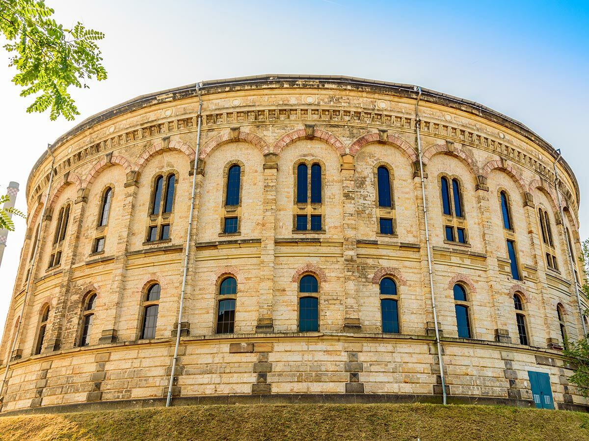 Massives zylindrisches Backsteingebäude mit Rundbogenfenstern auf einem Grashügel unter blauem Himmel. Historische Architektur.