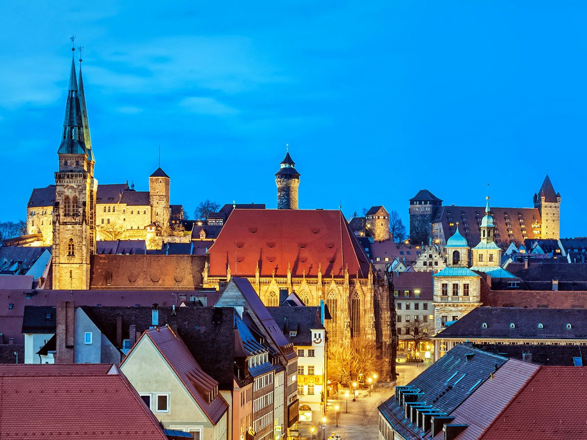 Panoramablick auf die historische Altstadt von Nürnberg am Abend mit Kaiserburg, Kirche St. Sebald und beleuchteten Dächern.