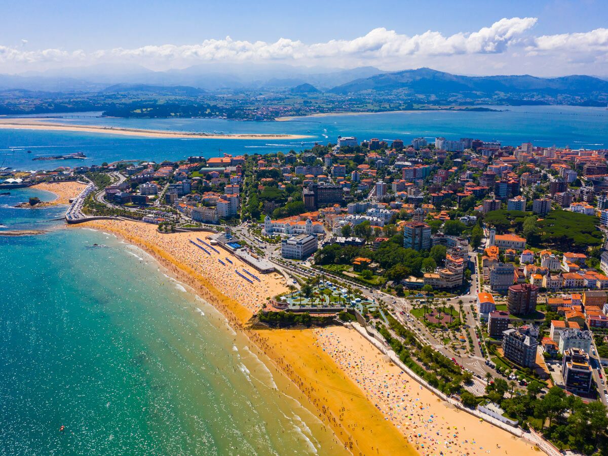 Luftaufnahme von Santanders El Sardinero Strand voller Menschen, dahinter die Stadt und eine Bucht mit Bergen.
