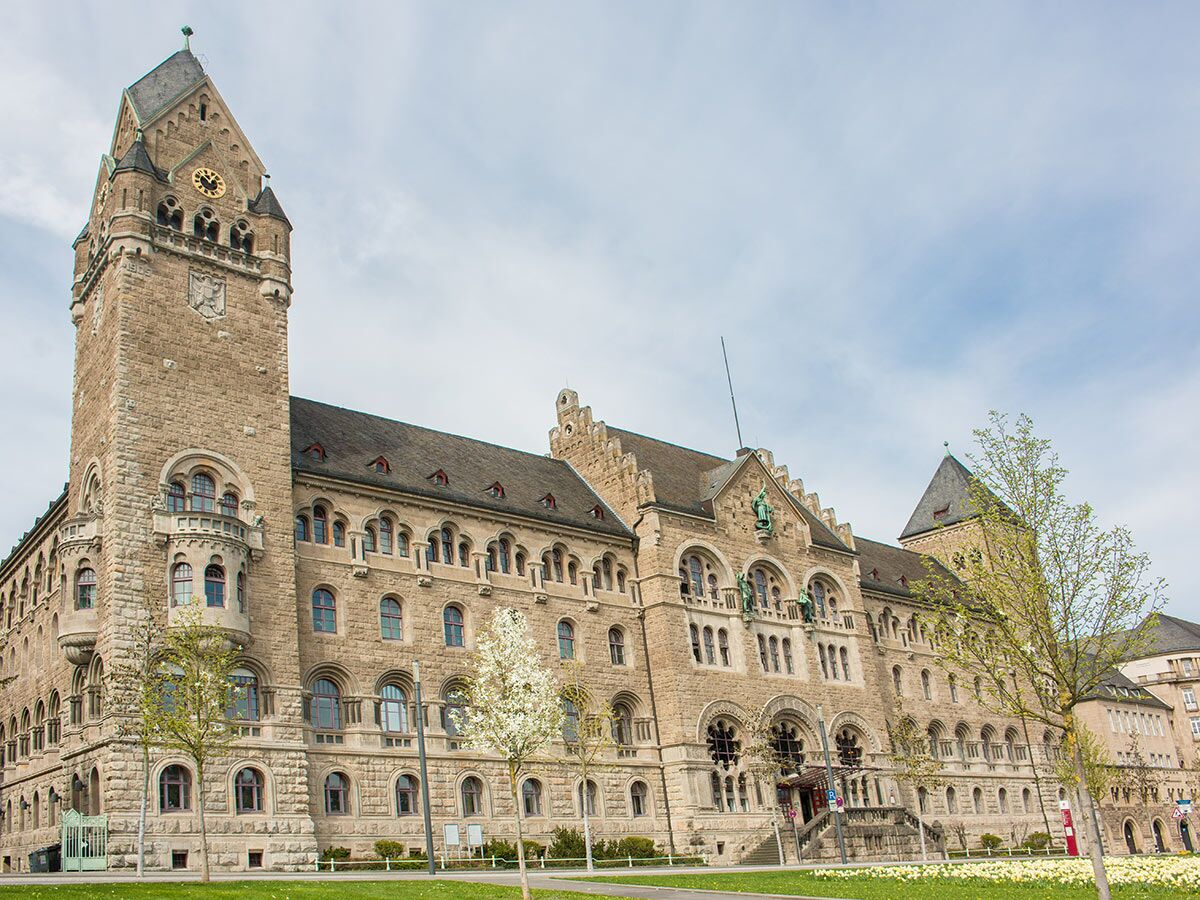 Das Oberlandesgericht Hamm: großes, historisches Steingebäude mit hohem Uhrenturm, vielen Fenstern und grüner Parkanlage im Frühling.