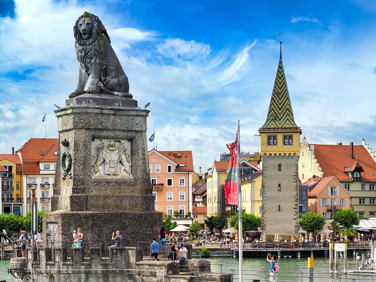 Der Hafen von Lindau am Bodensee mit dem Mangturm Leuchtturm und der bayerischen Löwenstatue unter blauem Himmel.