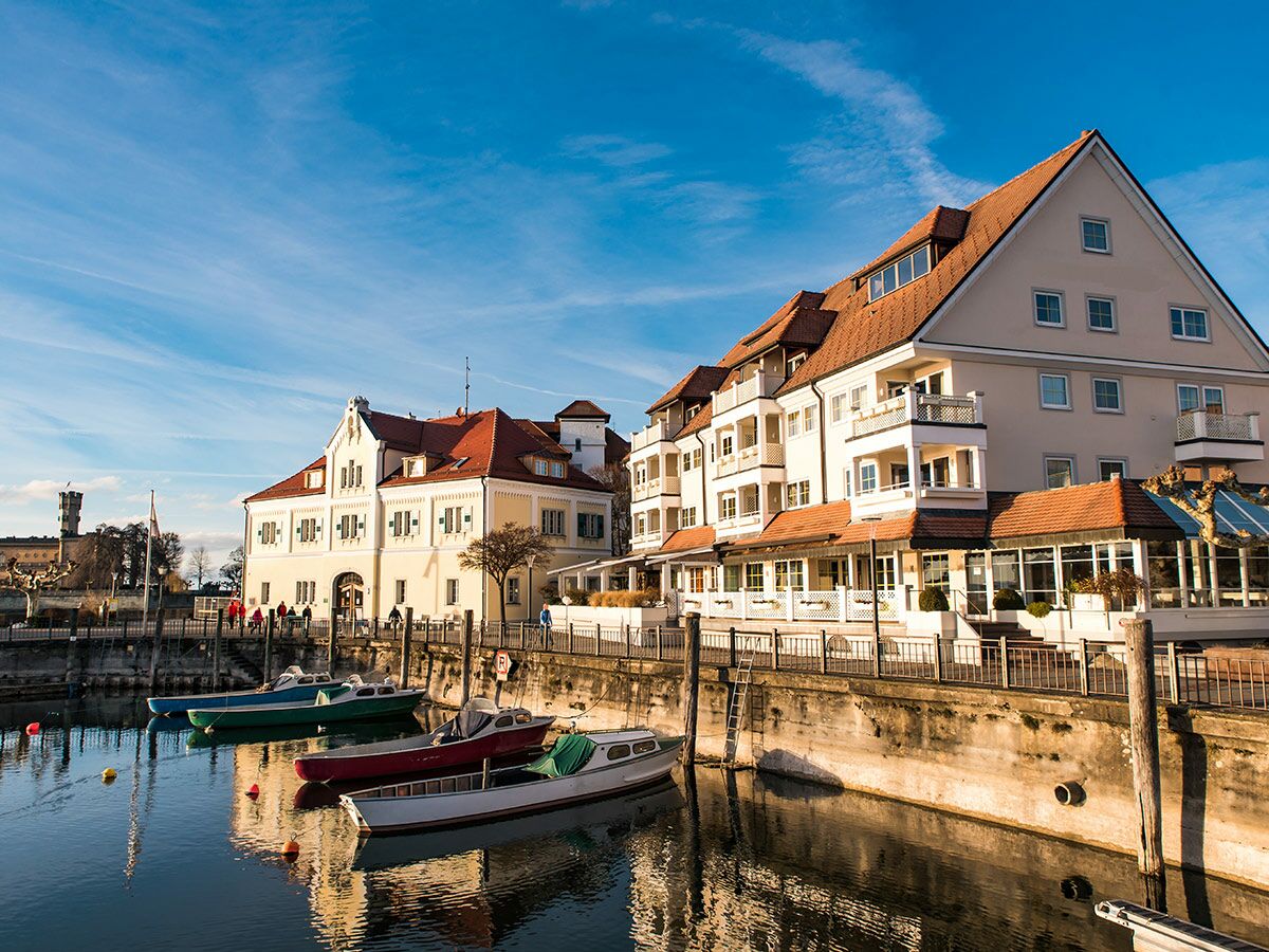 Malerische Hafenstadt am Bodensee mit traditionellen Gebäuden, roten Dächern und kleinen Booten im Hafenbecken an einem sonnigen Tag.