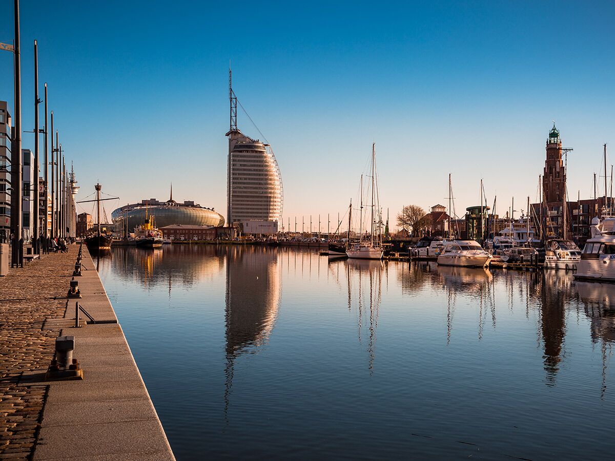 Panoramablick auf den Hafen von Bremerhaven mit Yachten, Segelbooten, modernem Klimahaus, Atlantic Hotel Sail City und historischem Leuchtturm.