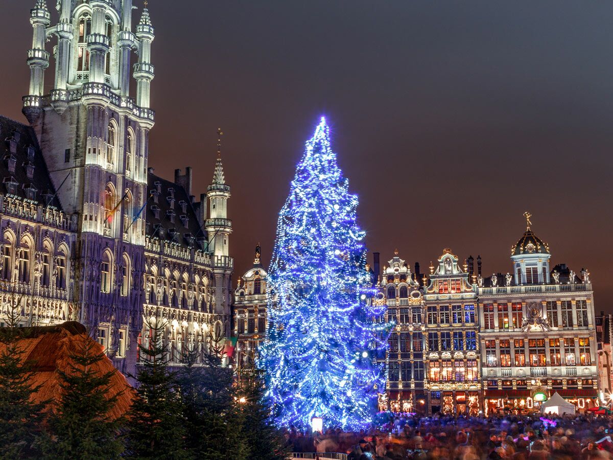 Beleuchteter blauer Weihnachtsbaum auf dem Grand-Place in Brüssel bei Nacht, umgeben von historischen Gebäuden und Menschen.