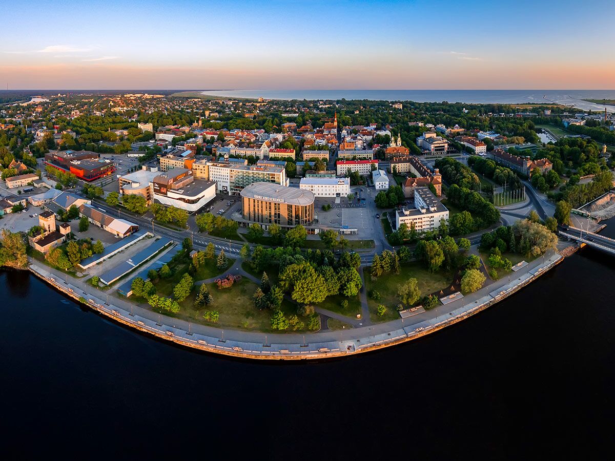Luftaufnahme der estnischen Stadt Pärnu mit Fluss, Promenade, Stadtgebäuden und Küste im Abendlicht.