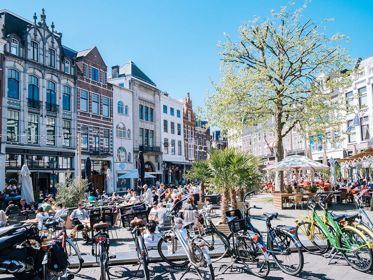 Belebtes Stadtplatz-Café in Europa mit Menschen auf Terrassen, historischen Gebäuden und vielen Fahrrädern an einem Sonnentag.