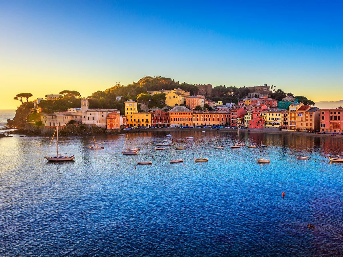 Panorama von Sestri Levante, Italien, mit bunten Häusern am Wasser, Booten in der ruhigen Bucht und lebhaftem Sonnenuntergang.