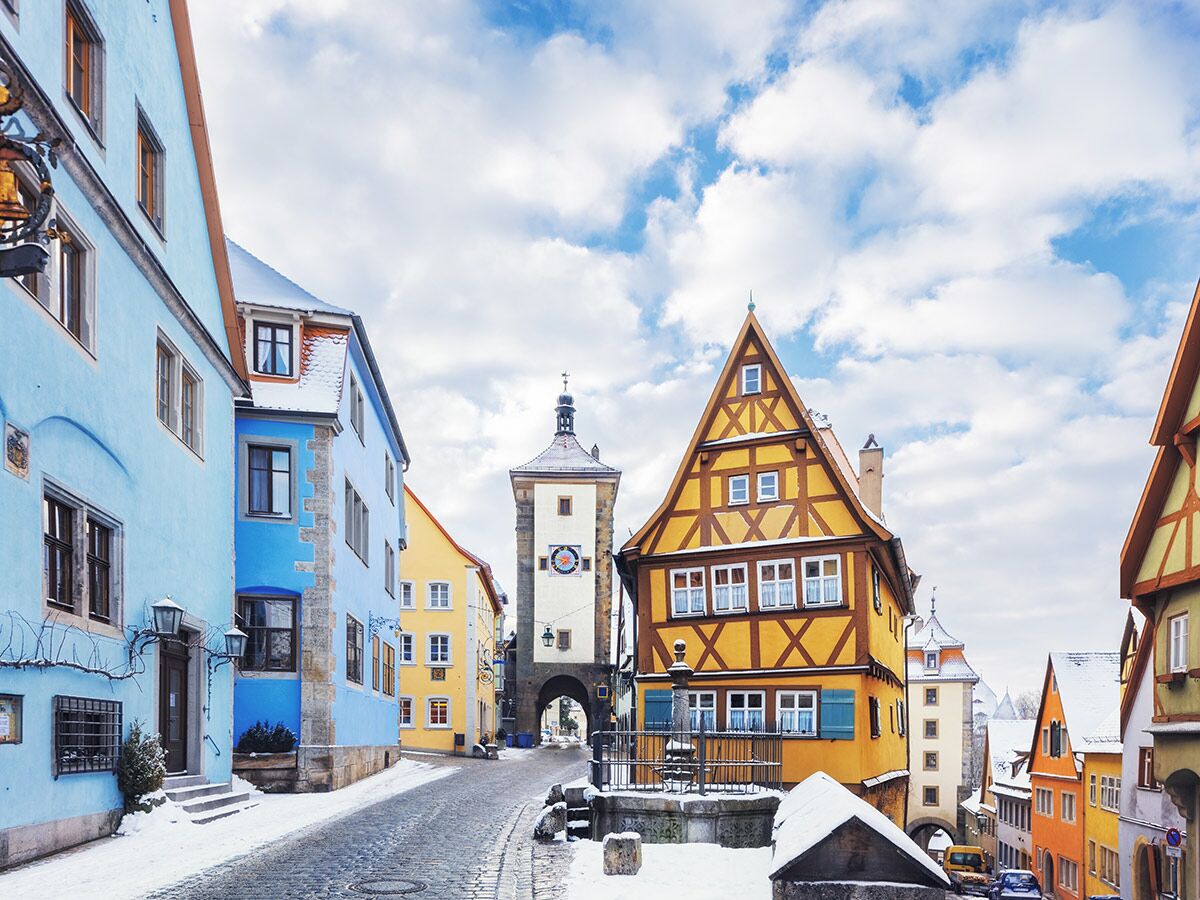 Winterliche Szene in Rothenburg ob der Tauber mit bunten Fachwerkhäusern, verschneiter Gasse und historischem Turm.